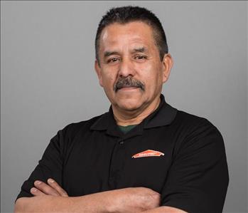 Male SERVPRO Technician with brown hair smiling in front of a gray background