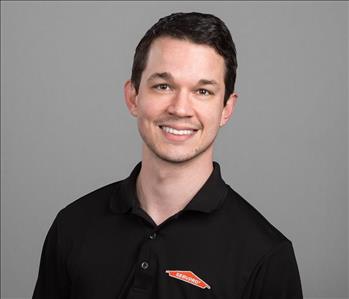 Male SERVPRO Technician with brown hair smiling in front of a gray background